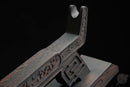 Supporto per katana in legno riccamente intagliato con motivi elaborati, ripreso da un'angolazione laterale su sfondo scuro. Supporto Katana Douu.