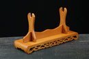 Supporto per katana in legno con base finemente intagliata, tonalità marrone calda, vista laterale su sfondo scuro. Supporto Katana Taiyou.