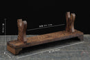 Supporto per katana in legno scuro rustico con due sostegni verticali su una superficie in legno testurizzata, leggermente angolato. Supporto Katana Heiwa.