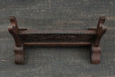 Supporto per katana in legno scuro con intagli elaborati, visto dall'alto su una superficie testurizzata. Supporto Katana Keshiki.