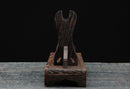 Supporto per katana in legno marrone intenso con parte superiore curva, venature elaborate e base robusta su una superficie grigia. Supporto Katana Mokuzai.