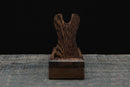 Vista frontale di un porta spada singolo in legno scuro con venature elaborate su sfondo rustico. Supporto Katana Heiwa.