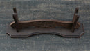 Supporto per katana in legno scuro con venature elaborate, visto dall'alto su una superficie testurizzata. Supporto Katana Otera.