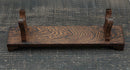 Supporto per katana in legno scuro con venature testurizzate, dotato di due sostegni verticali su una superficie rustica. Supporto Katana Heiwa.