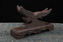 Supporto per katana in legno scuro con sagoma d'aquila, su una superficie rustica, vista laterale. Supporto Katana Washi.