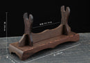Supporto per katana in legno rustico con estremità intagliate, finitura in legno scuro, dimensioni indicate, appoggiato su una superficie testurizzata. Supporto Katana Mokuzai.