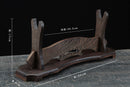 Supporto per katana in legno con finitura marrone scuro, che mostra un design decorato e le dimensioni misurate, inclinato su una superficie rustica. Supporto Katana Ote...