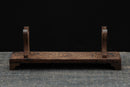 Supporto per katana in legno tinto scuro su una superficie testurizzata, con curve decorative e base robusta. Supporto Katana Heiwa Supporto Katana Hwa ...