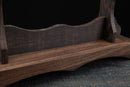 Primo piano di un supporto per katana in legno scuro con bordi curvi su una superficie testurizzata, che ne mette in risalto venature e lavorazione. Supporto Katana Mokuzai.