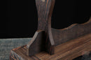 Primo piano di un supporto per katana in legno scuro con venature lisce e curve eleganti su una superficie rustica. Supporto Katana Mokuzai.