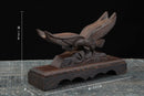 Supporto per katana in legno decorato con un'aquila, intagliato in legno scuro, visto di lato su una superficie testurizzata. Supporto Katana Washi.