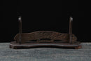 Vista frontale di un supporto per katana in legno scuro con base curva su sfondo scuro. Supporto Katana Otera.